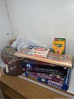 Photo showing DVD game box, Mille Bornes card game, wooden ring toss game, Crayola crayons, and sports balls on shelf
