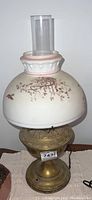 Front view of the electric lamp showing the large round glass floral shade with pink trim and brown flower designs and ornate metal base with push on/off button.