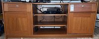 Front view of wooden media cabinet, showing two locking drawers on top with metal pulls and keyholes, sliding shelves in middle section and closed cabinet doors below.