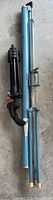 Blue metal portable projection screen case and folded Manfrotto tripod stand placed side by side on a concrete floor.