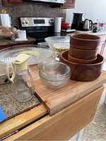 Photo showing glass soy sauce bottle with plastic lid, nested wooden bowls, clear glass bowls of various sizes on wooden cutting board and kitchen counter.