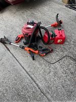 Full view of Black and Decker shop vac, weed trimmer/edger with battery and two plastic gas cans on concrete surface.