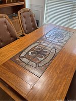 Close-up of the center tile inset on wooden dining table, showing geometric earth-tone pattern.