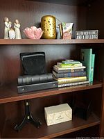 Wooden bookshelf with shelves containing books, figurines, candle holder, tea mugs box, bookends, and earphones.