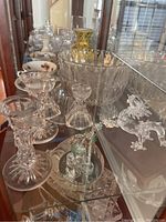 Shelf with assorted glass candlesticks, crystal figurines, gold decorated vase, bowls and Lefton china tea cups visible
