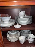 Photo showing stacked dinner plates, cups stacked on plates, and gravy boat on top shelf with salad plates below.