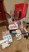Photo of assorted Christmas wrapping supplies, gift bags, holiday cards, colored pens, photo albums, and ceramic mug on carpet floor