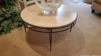 Full view of round coffee table with beige stone top and metal base, placed on carpet near furniture.