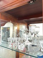 Crystal and glass figurines, perfume bottle, wine glasses, and bowls displayed on a glass shelf.