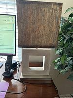 Front and side views of contemporary desk lamp showing silver and acrylic square hollow base with brown textured square shade on top, lamp cord visible.