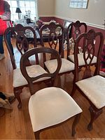 Five dining room chairs shown from front and side views in a dining room setting, illustrating the four matching chairs and one differing chair with white upholstered seats.