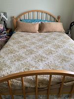 Front view of full size pine bed frame made of light wood with curved headboard and footboard, topped with beige gold quilted comforter and two long beige pillows.