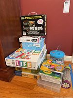 Photo showing the stacked items including The Game of Life board game, Star Wars 500 piece puzzle, a 1000 piece puzzle, assorted markers and scented markers, and the hermit crab blue container kit.