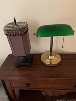 Two lamps on wooden table, brass/silver desk lamp with green glass shade on right, small wooden table lamp with purple fabric shade and beads on left