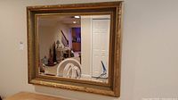Full view of rectangular wall mirror with gold and grey ornamental frame and beveled glass edges.