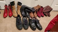 Photo showing all seven pairs of boots and shoes in the lot, arranged on a beige carpet.