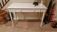 Front view of the white wooden table showing drawer and legs.
