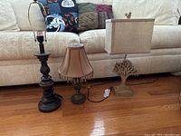 Three table lamps shown together in one image on a wooden floor in front of a beige couch, showing various shades and lamp base styles.