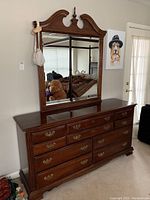 Full frontal view of the triple dresser with mirror showing dark wood finish, brass handles, and decorative mirror arch.