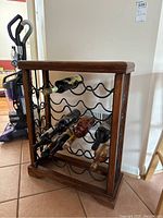 Front angle showing wooden frame with black metal bottle holders holding several wine bottles.