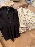 Two coats laid on carpeted floor, one black with fur collar, one floral pattern.