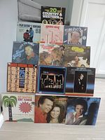 Photo of all 13 vinyl LP covers arranged and standing against a wall, showing titles and visible cover art.
