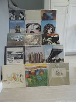 Photo shows stacked LP albums, mostly 70's rock, with some visible titles and cover art depicting various bands and artists.