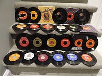 Overview of 24 various 45 RPM vinyl records arranged on carpeted stairs including different colored labels and a storage box.