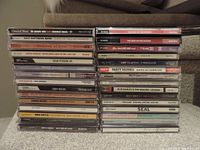 Photo of 30 CDs arranged in three stacks showing spines with album titles and artist names, in jewel cases, various genres represented