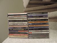 Photo showing 30 CDs stacked in three columns on carpet with a couch and stairs in background.