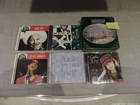 Photo of six Christmas music CDs including a green metal tin box set, and CDs by Burl Ives, Stevie Wonder, Michael Bublé, Charlotte Church, and a Blue Yule album.