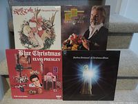 Photo showing four Christmas-themed vinyl LP records stacked on stairs: Frankie & Dolly, Kenny Rogers, Elvis Presley Blue Christmas, and Barbara Streisand Christmas album.