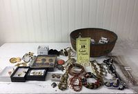 A vintage basket filled with assorted costume jewelry items including earrings, pendants, bracelets, and necklaces spread out on a white surface.