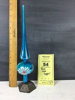 Front view showing blue plastic tree topper with floral design next to a ruler for scale and yellow Maxsold tag with lot details.