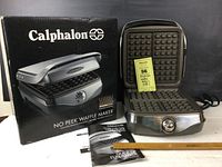 Calphalon No Peek Waffle Maker with original box and instruction manual; waffle maker is open showing cooking grids and front dial.