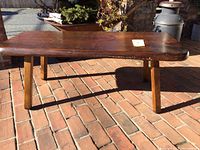 Full view of vintage free form pine slab table showing rectangular top with curved edges and four wooden legs on brick floor.