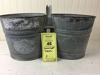 Front angled view of the pair of connected galvanized metal pails showing shared handle and signs of patina.