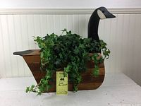 Front angled view of wooden goose planter holding artificial ivy plant, showing wood grain and black painted goose head.