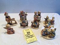 Full view of all 8 Hummel figurines arranged on white surface including children, angel scenes, and boy and girl on fence.