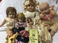 Seven mixed composition and porcelain/plastic dolls arranged on white cloth background showing size and condition.