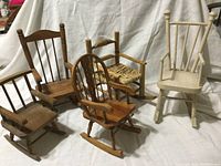 Five different wooden doll rocking chairs arranged on white fabric background showing variety in height, style, and finish.