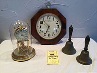 Lot overview showing the German dome clock in glass dome, wall clock, and two school bells.
