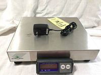 Oblique front view showing stainless steel platform, display module, and AC adapter on top.