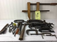 Front view showing entire collection of vintage clamps and hand tools laid on white surface.