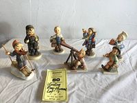 All seven Hummel boys figurines displayed together on cloth background per seller overview.