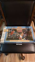 Photo of the sealed game box positioned on a chair showing front cover artwork and title.
