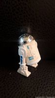 Side angle of the vintage R2-D2 figure showing white plastic legs, silver head and worn blue printed decals on the body.