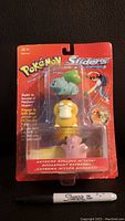 Front view of original 1999 Pokemon Sliders toy set in sealed packaging, showing Bulbasaur, Psyduck, and Jigglypuff figures with Sharpie pen for scale.