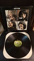 Front cover of Let It Be album with vinyl record on white paper sleeve, showing images of John Lennon, Paul McCartney, George Harrison, and Ringo Starr.