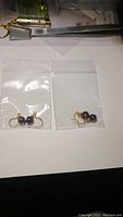 Two small ziplock bags each containing a pair of garnet sphere earrings with brass hooks on a white surface.